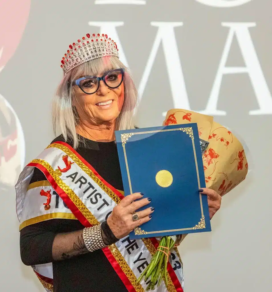 Contemporary artist Patricia Karen Gagic wearing an Artist of the Year sash and holding a blue and gold award plaque.
